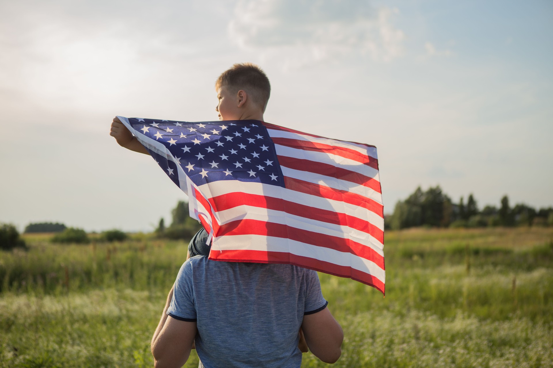 Little boy lets the american flag fly in his hands on the wind at the green field. Patriotic family celebrates usa independence day on 4th of July. Constitution and Patriot Day.