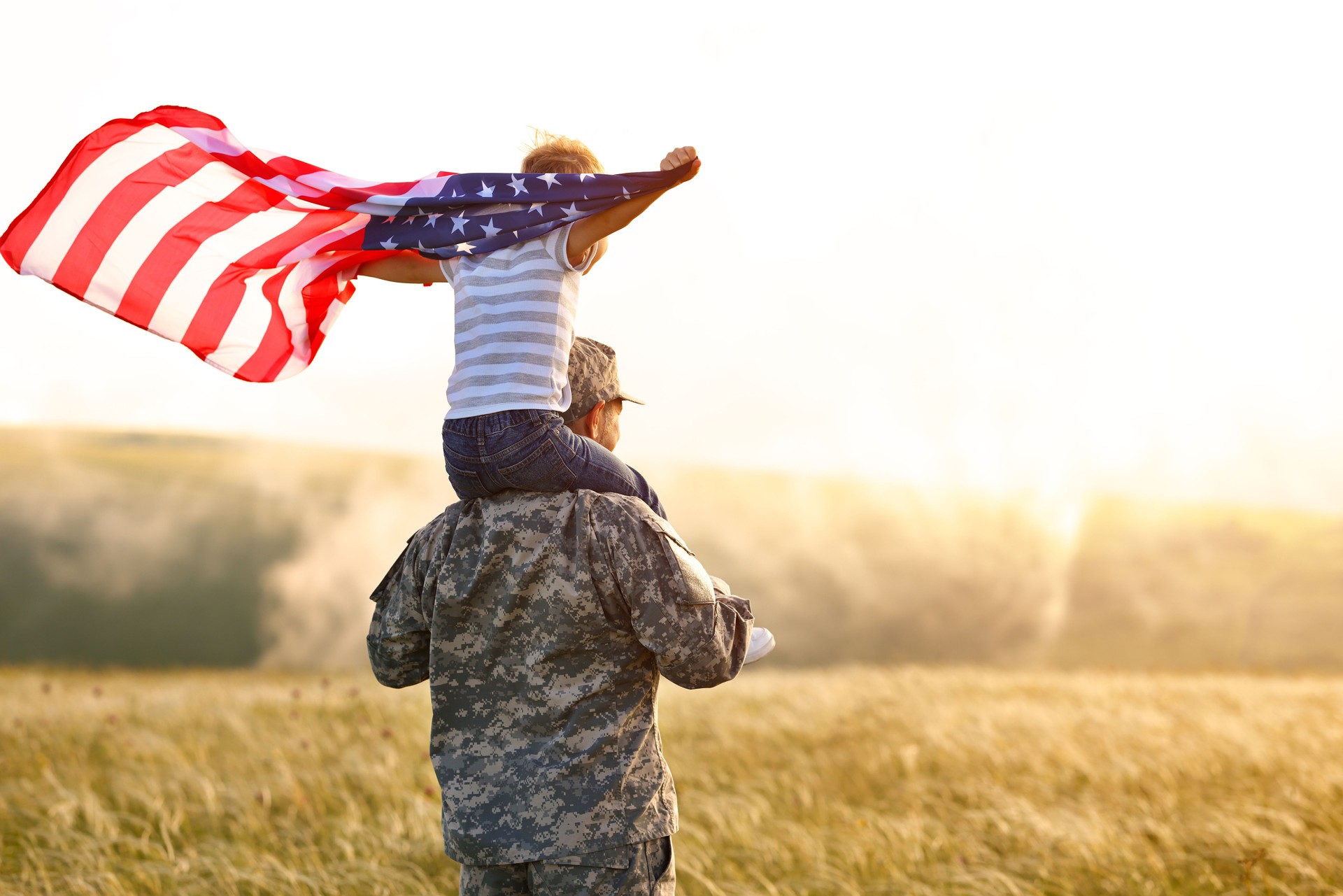 Excited child sitting with american flag on shoulders of father reunited with family