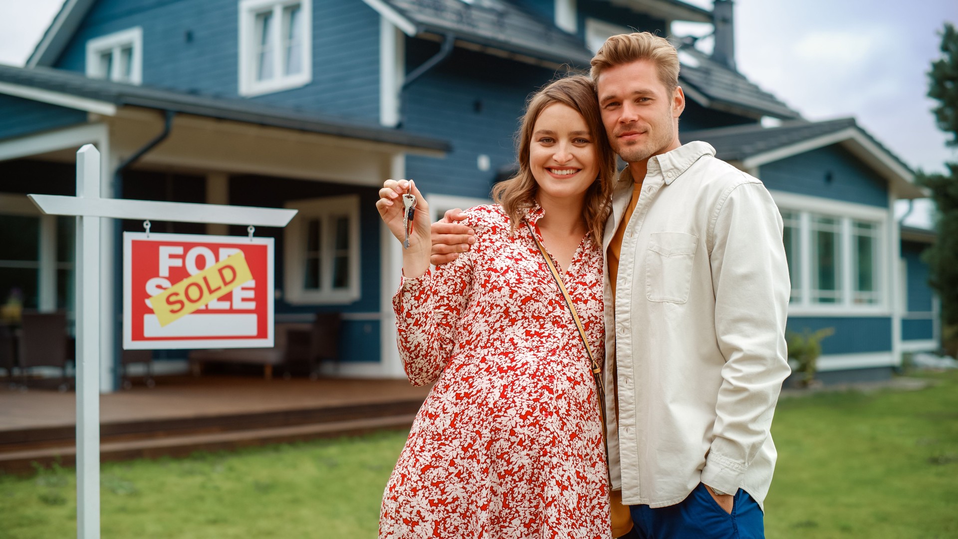 Portrait of a Beautiful Young Couple in Love Standing in Front Their New Home. Successful Homeowners Looking at Camera and Smile. Female in a Dress Expecting a Baby. Real Estate Housing Market Concept